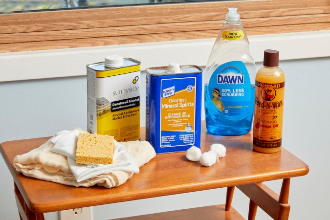 Materials needed to clean wood furniture (including mineral spirits and dish soap) collected on a small wood table.