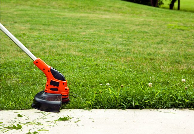 Red lawn edger runs along a driveway cutting grass beyond the driveway.