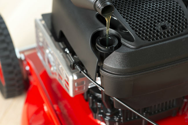 Someone out of frame pours oil into a red lawnmower.