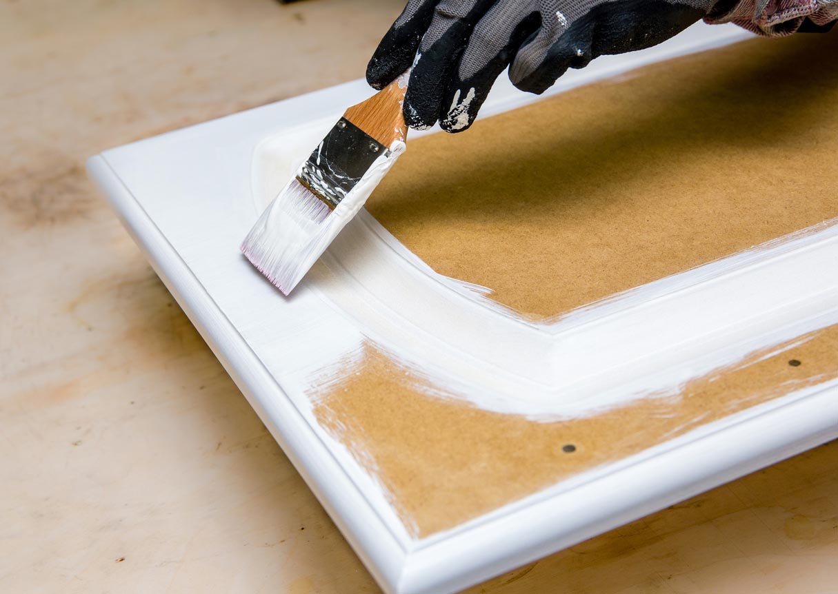 Closeup of person painting the back of a wooden cabinet door white.