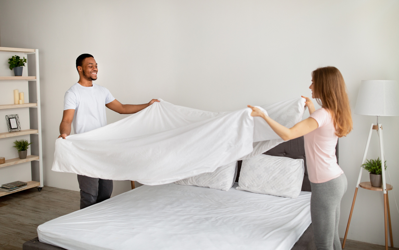 Young couple making the bed by holding a sheet over the bed.