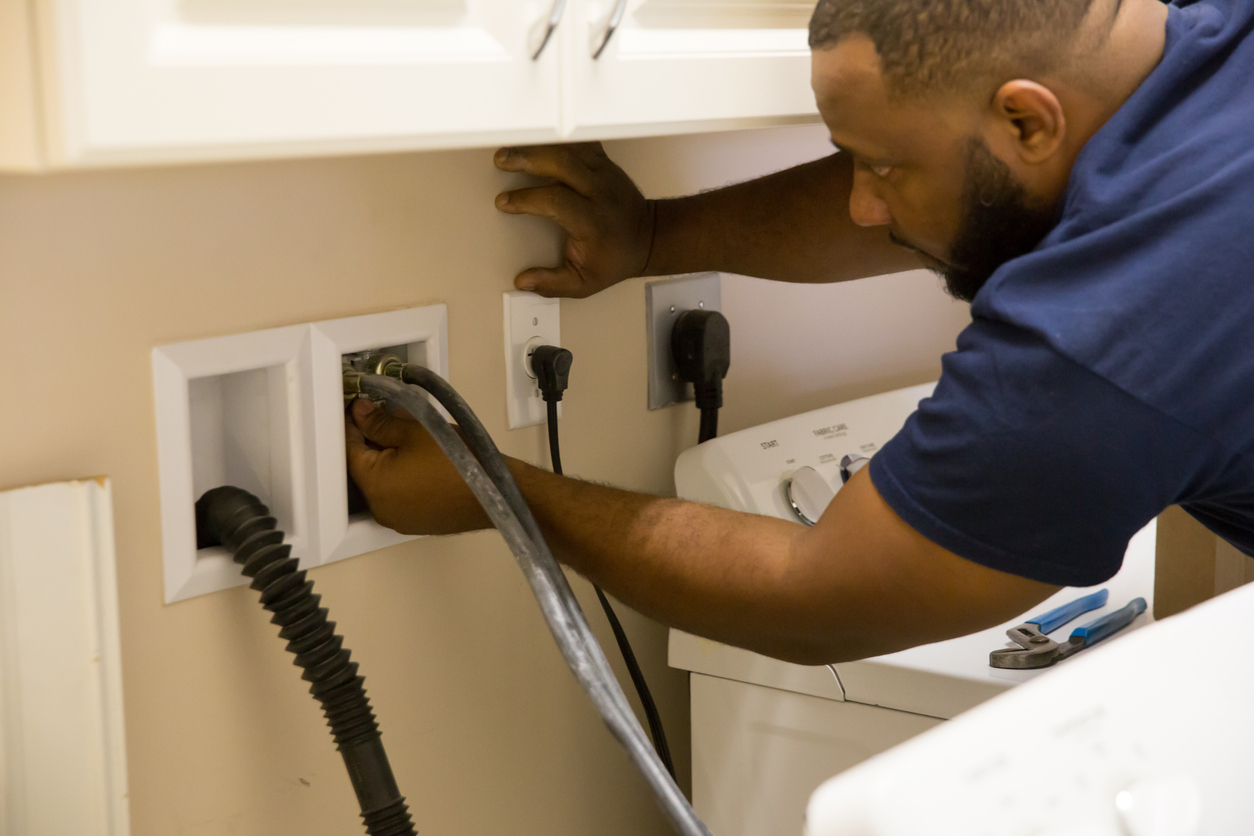 Man inspecting hose connections at wall behind the washing machine.